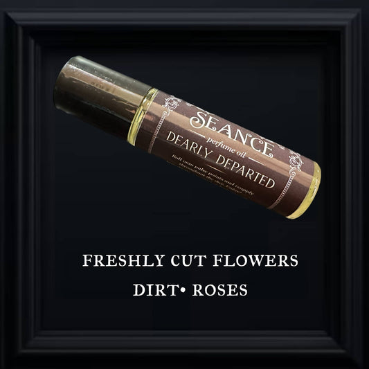 Picture of a glass roller-ball perfume vial titled Dearly Departed on a black background, with the words freshly cut flowers, dirt, and roses written underneath.