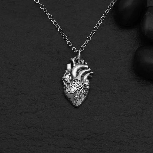 A sterling silver charm in the shape of an anatomically correct human heart, hanging from a silver chain. 